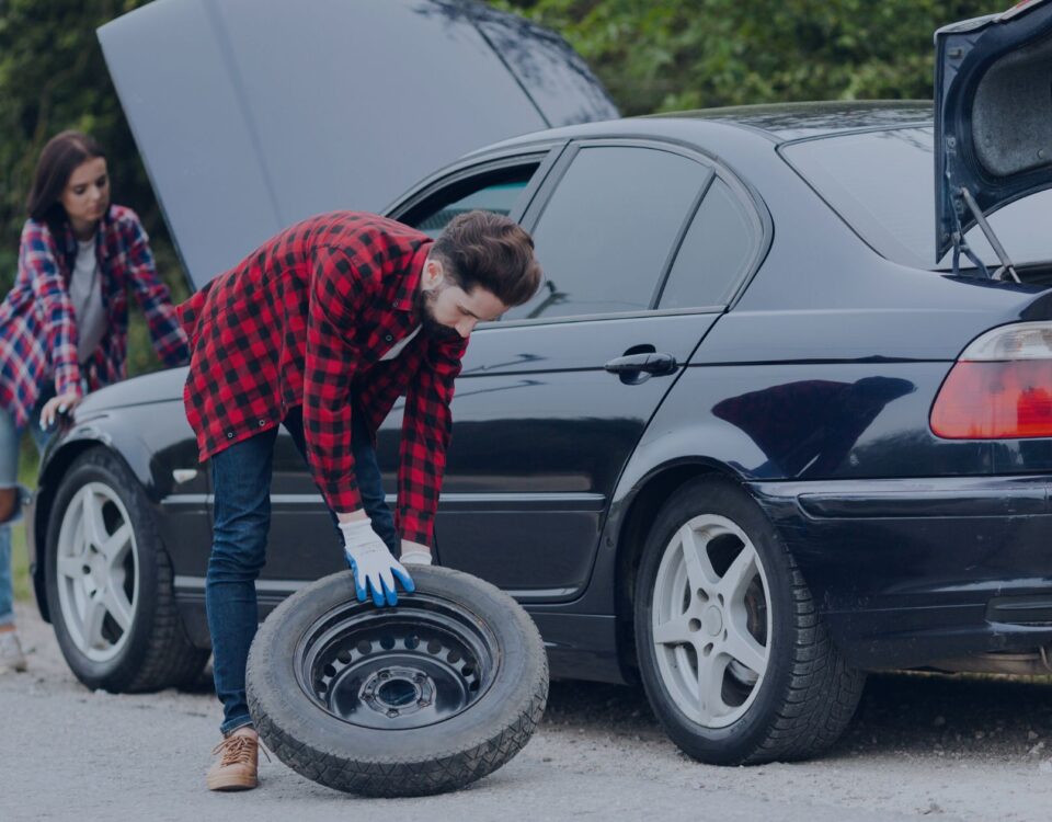 A tyre Mechanic bent down to pick the new tyre to install in the car-The Most Professional tyre rescue services Denton - Greater Manchester in 2024